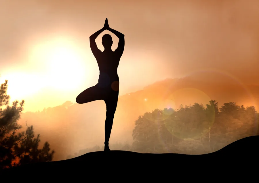 A person practising a standing yoga pose at sunrise